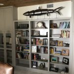 Gray and white wooden book shelf with large wooden fish sculpture.