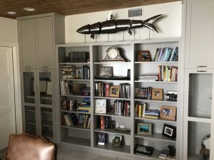 Gray and white wooden book shelf with large wooden fish sculpture.